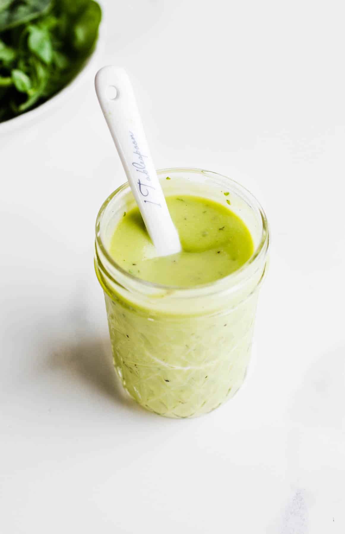 Green avocado dressing in a glass jar with a white ceramic spoon dipped in the middle.