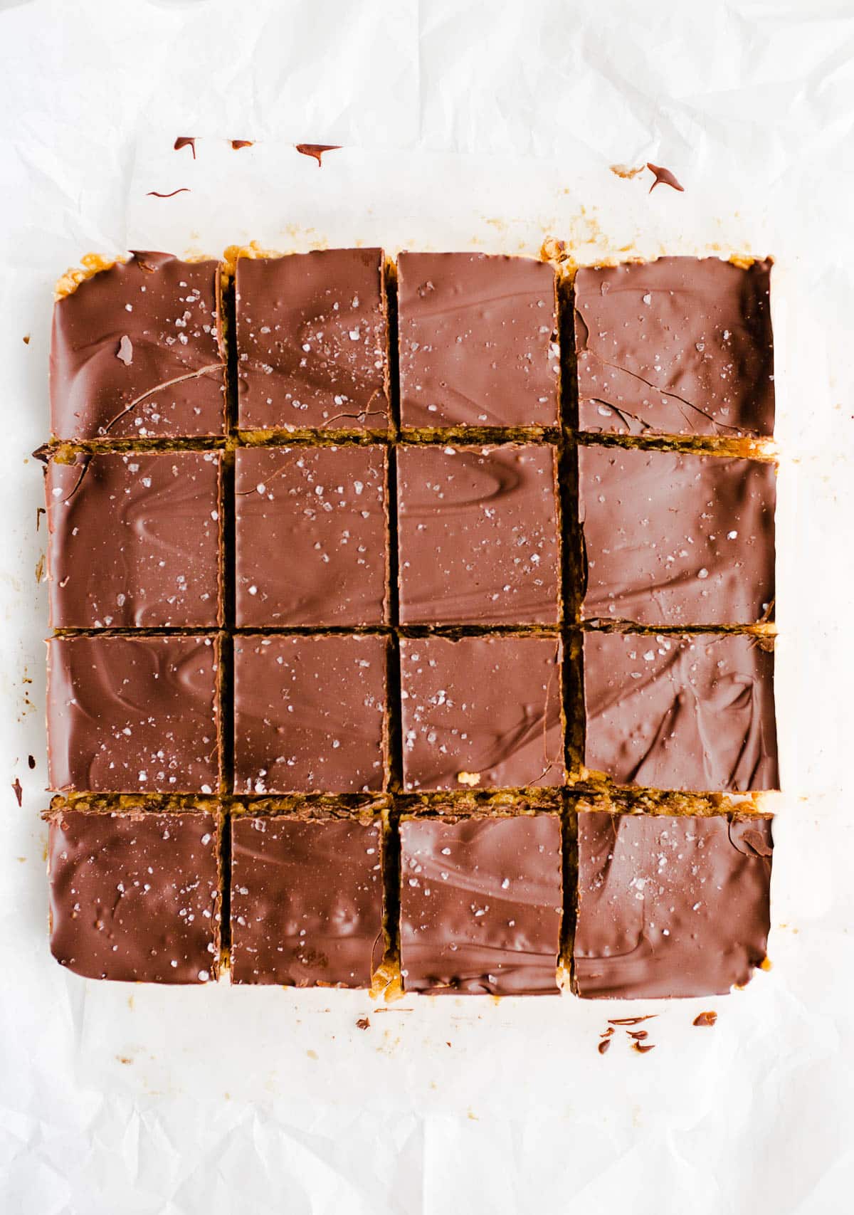 Chocolate covered peanut butter cereal bars freshly sliced on top of white parchment paper.