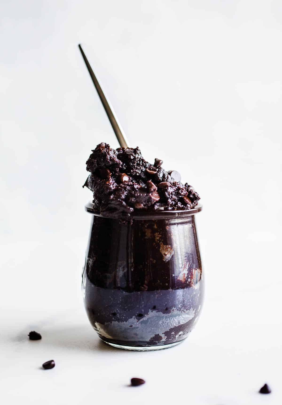 Edible brownie batter with chocolate chips in a glass jar with spoon.