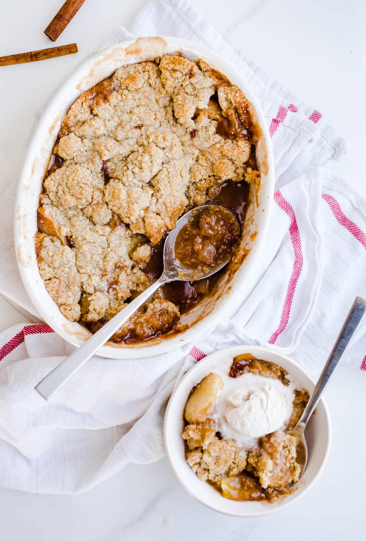Freshly baked apple crumble in a white dish next to a small bowl with apple crumble and ice cream. 
