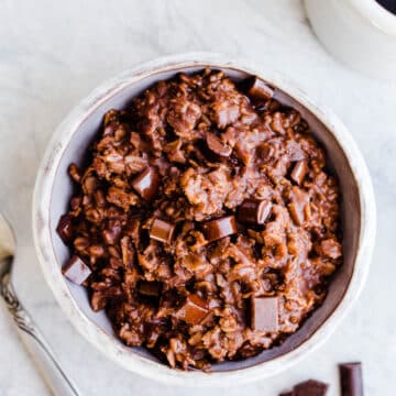 A bowl of chocolate oatmeal topped with chocolate chunks.