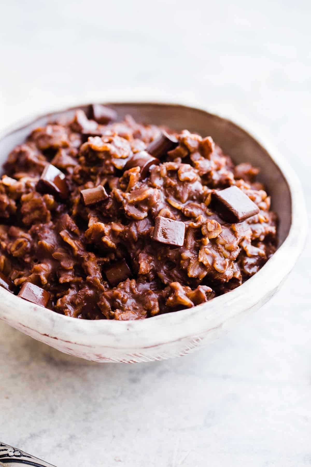 A bowl of chocolate oatmeal with melted chocolate chunks on top.