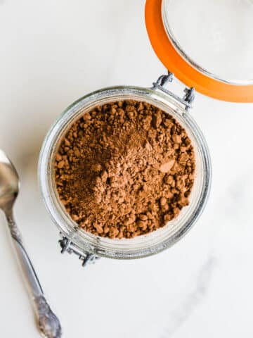 A glass canister of unsweetened cocoa powder.