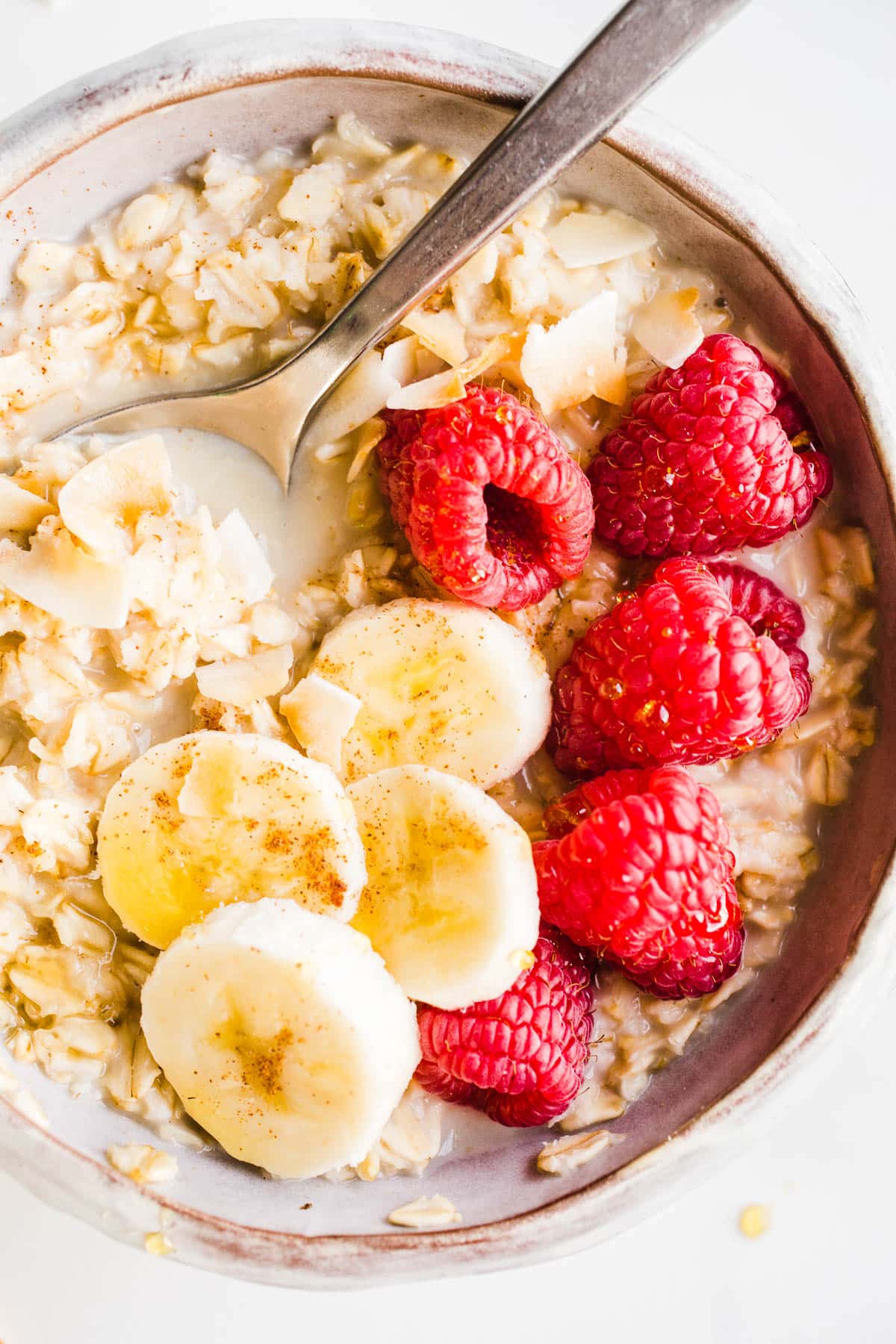 A bowl full of oatmeal topped with raspberries, coconut flakes, and banana slices. 