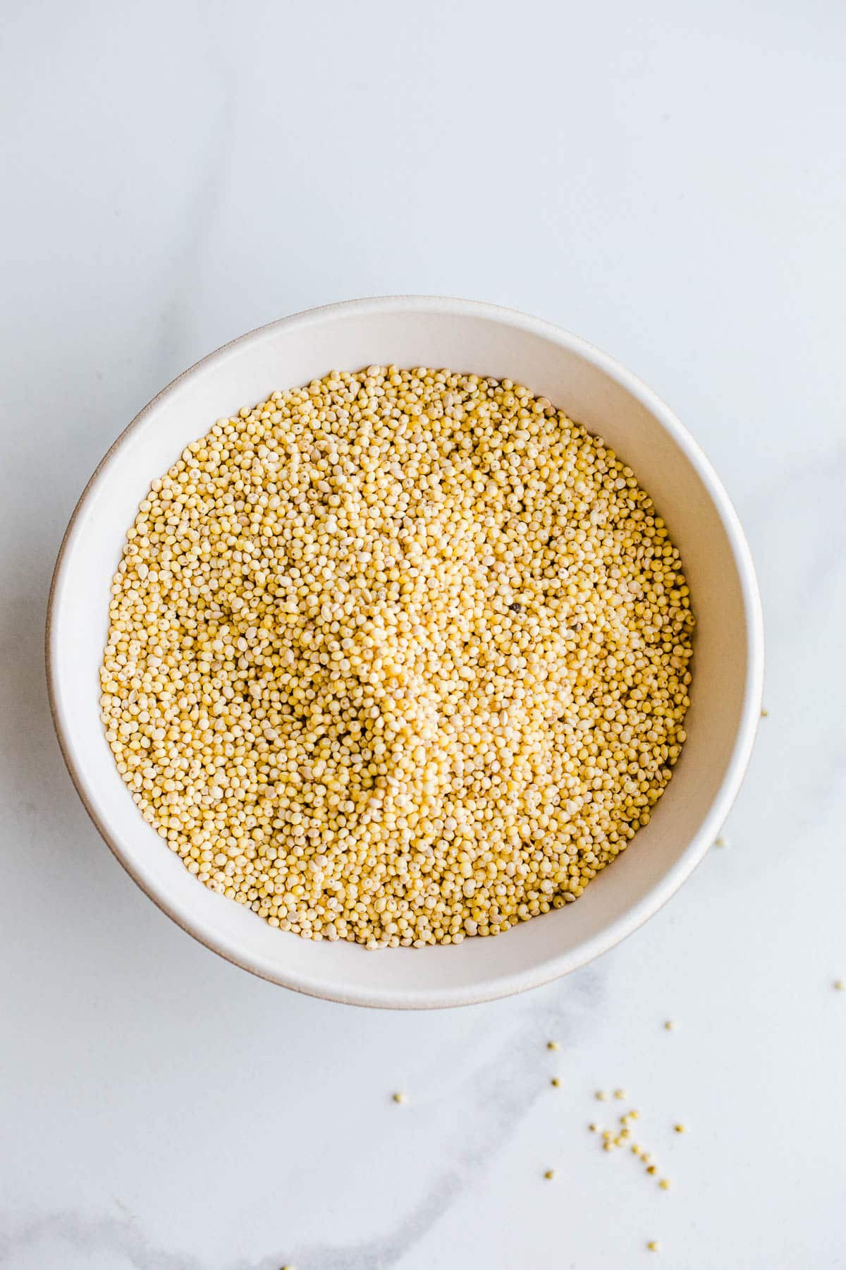Whole millet grains in a small white bowl.