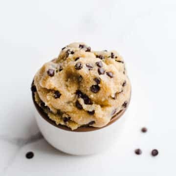 Dough with chocolate chips in a small white cup.