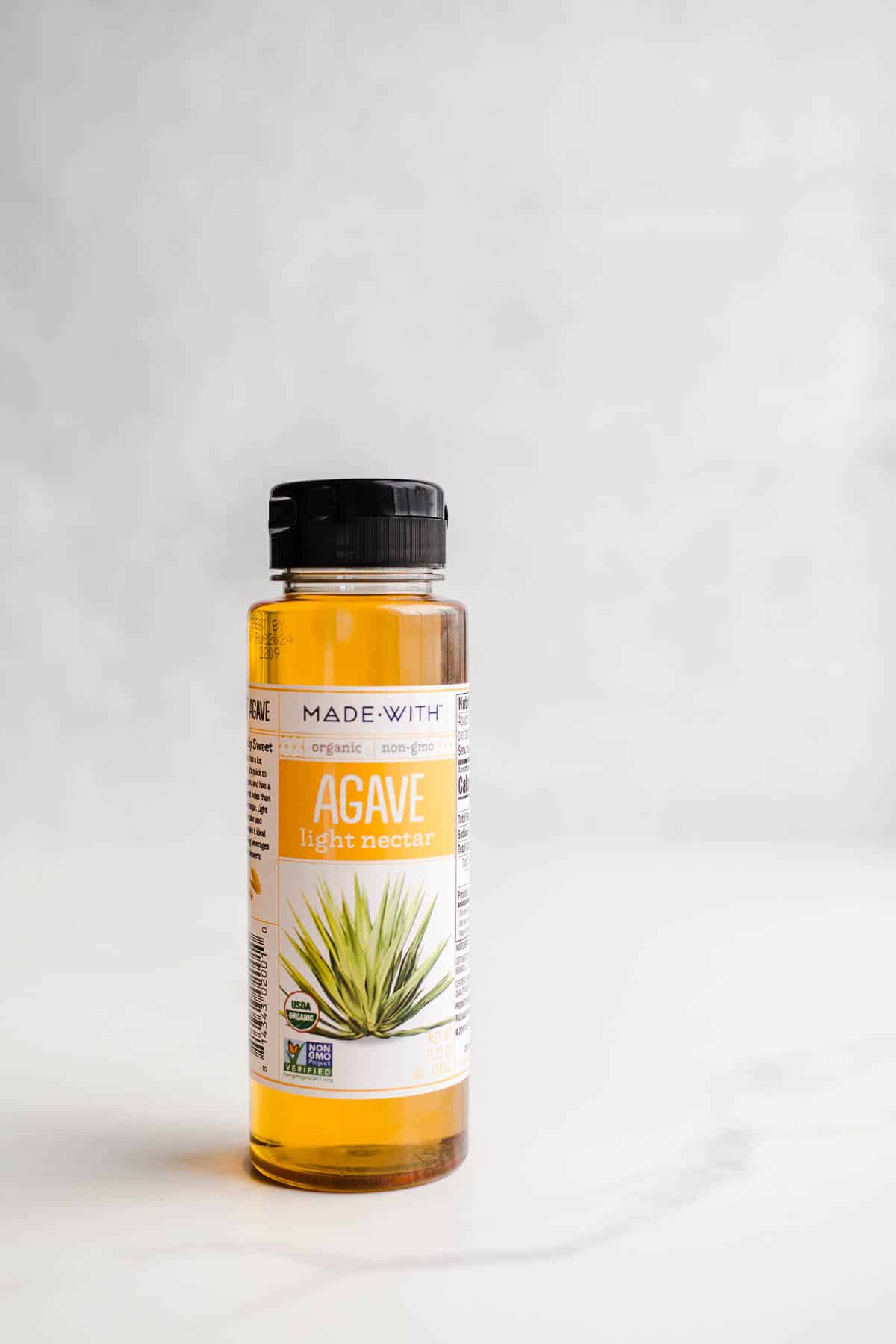 A slim bottle with light golden syrup on a marble surface.