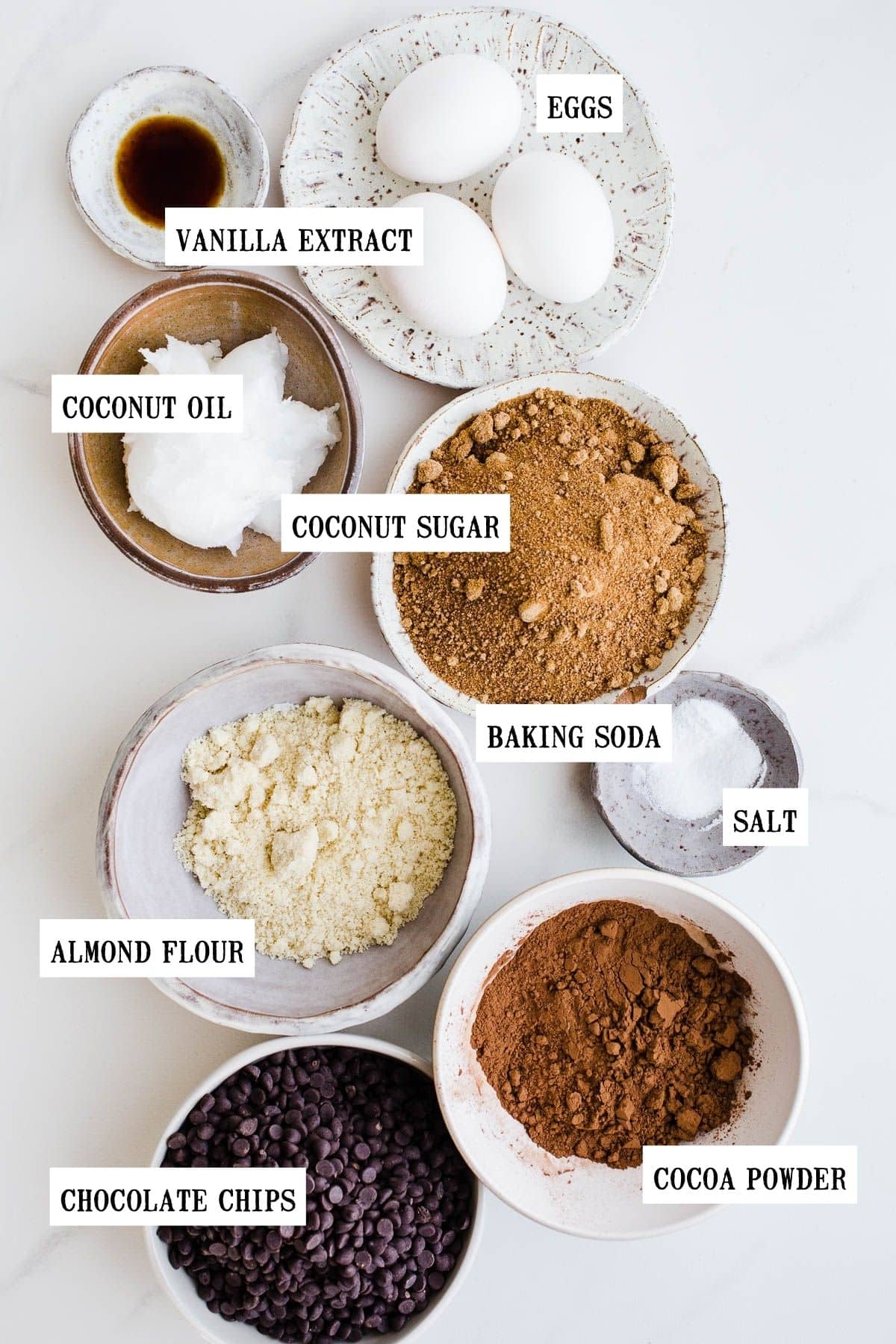 Ingredients to make gluten-free dairy-free brownies set on a marble surface in small bowls.