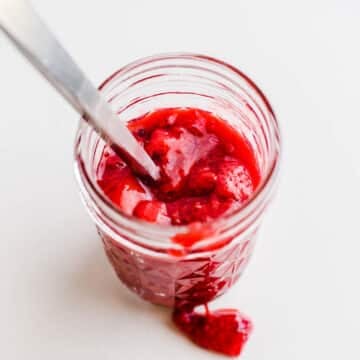 Bright red fruit compote in a glass jelly jar.
