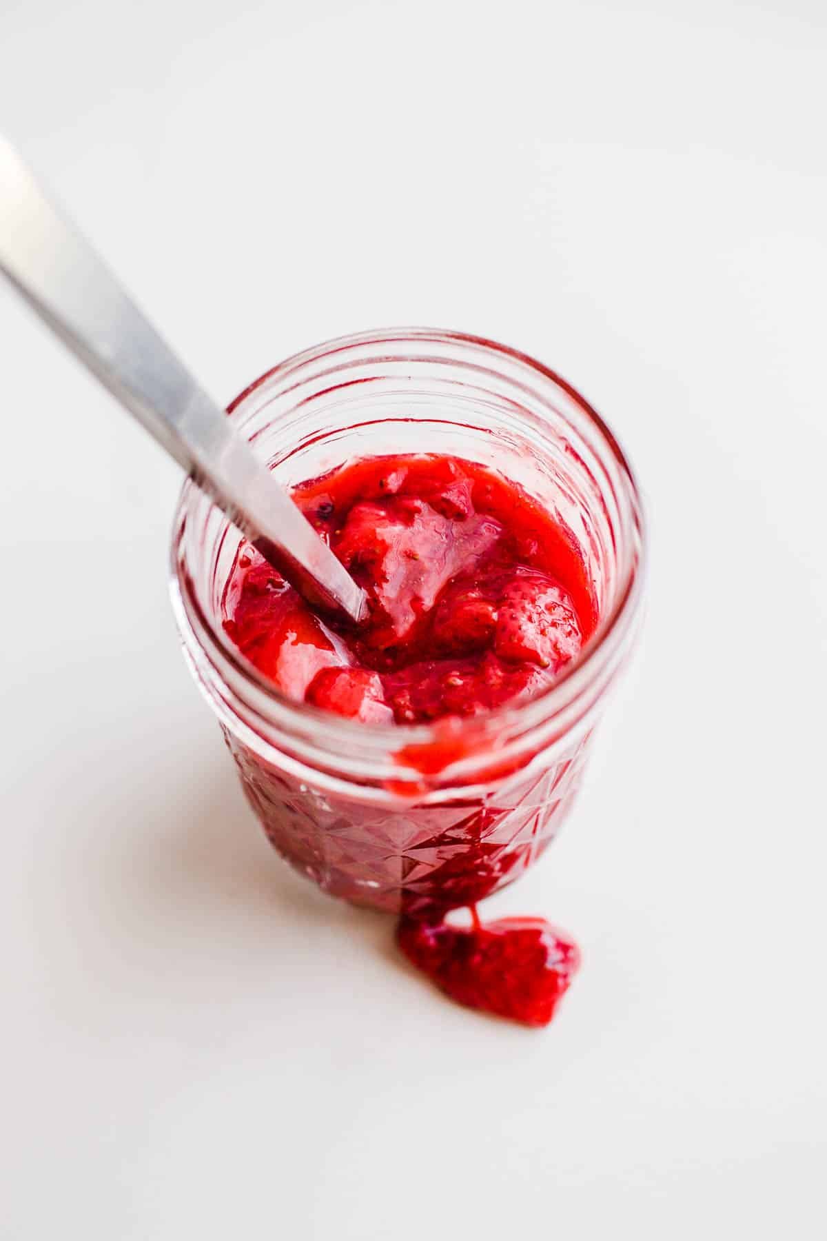 Bright red fruit compote in a glass jelly jar.