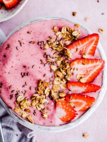 A pink smoothie bowl with fruit and granola.