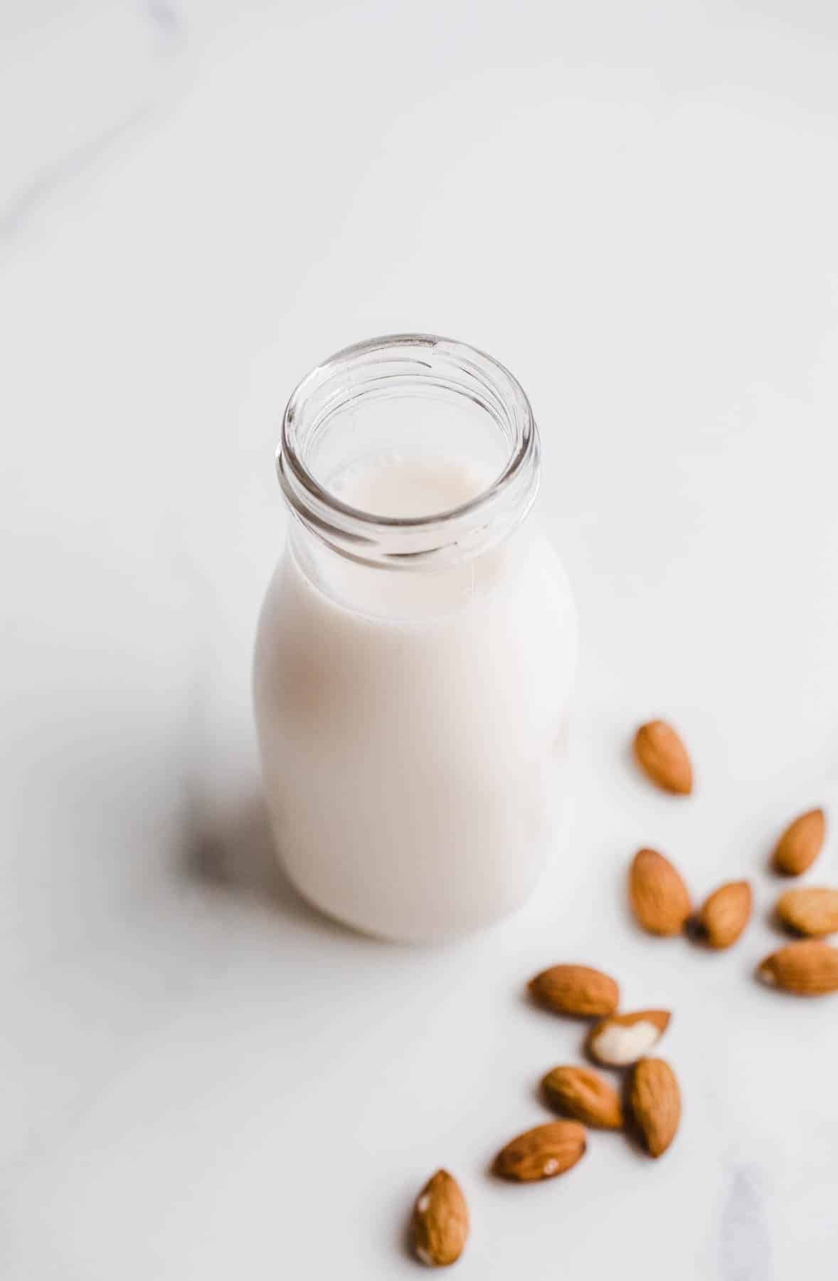 A bottle filled with almond milk next to scattered almonds.