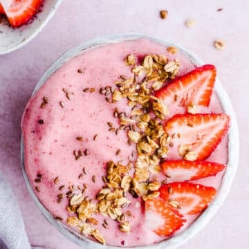 A smoothie bowl topped with granola and strawberries.