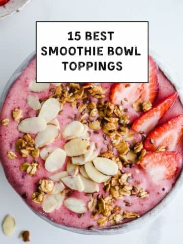 A bowl full of strawberry smoothie topped with granola and nuts.