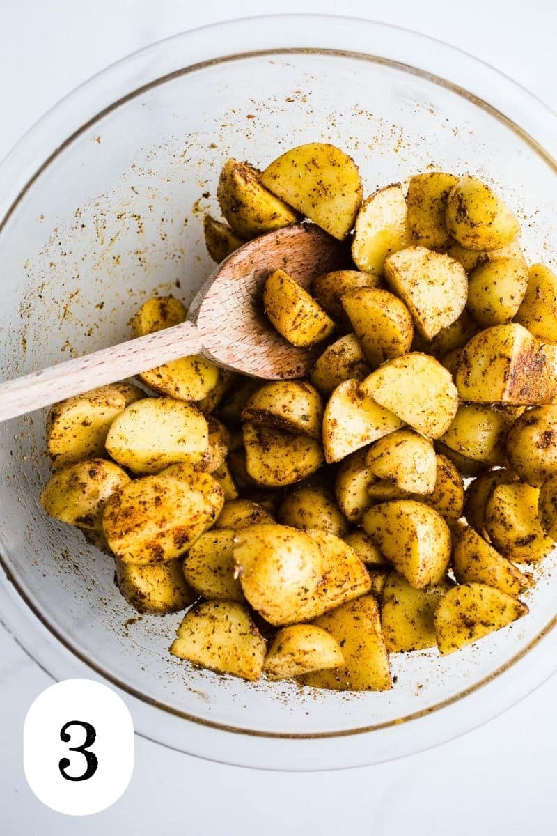 Potatoes tossed with oil in a bowl.
