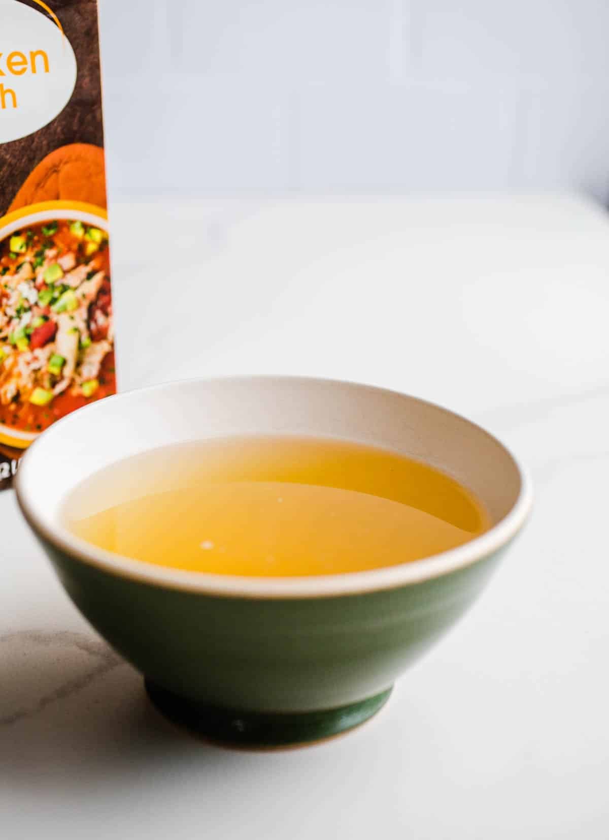 A green bowl with yellow liquid on a marble surface.