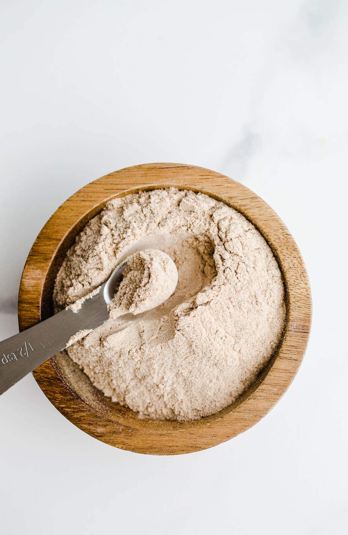 A wooden bowl filled with powder with a spoon.