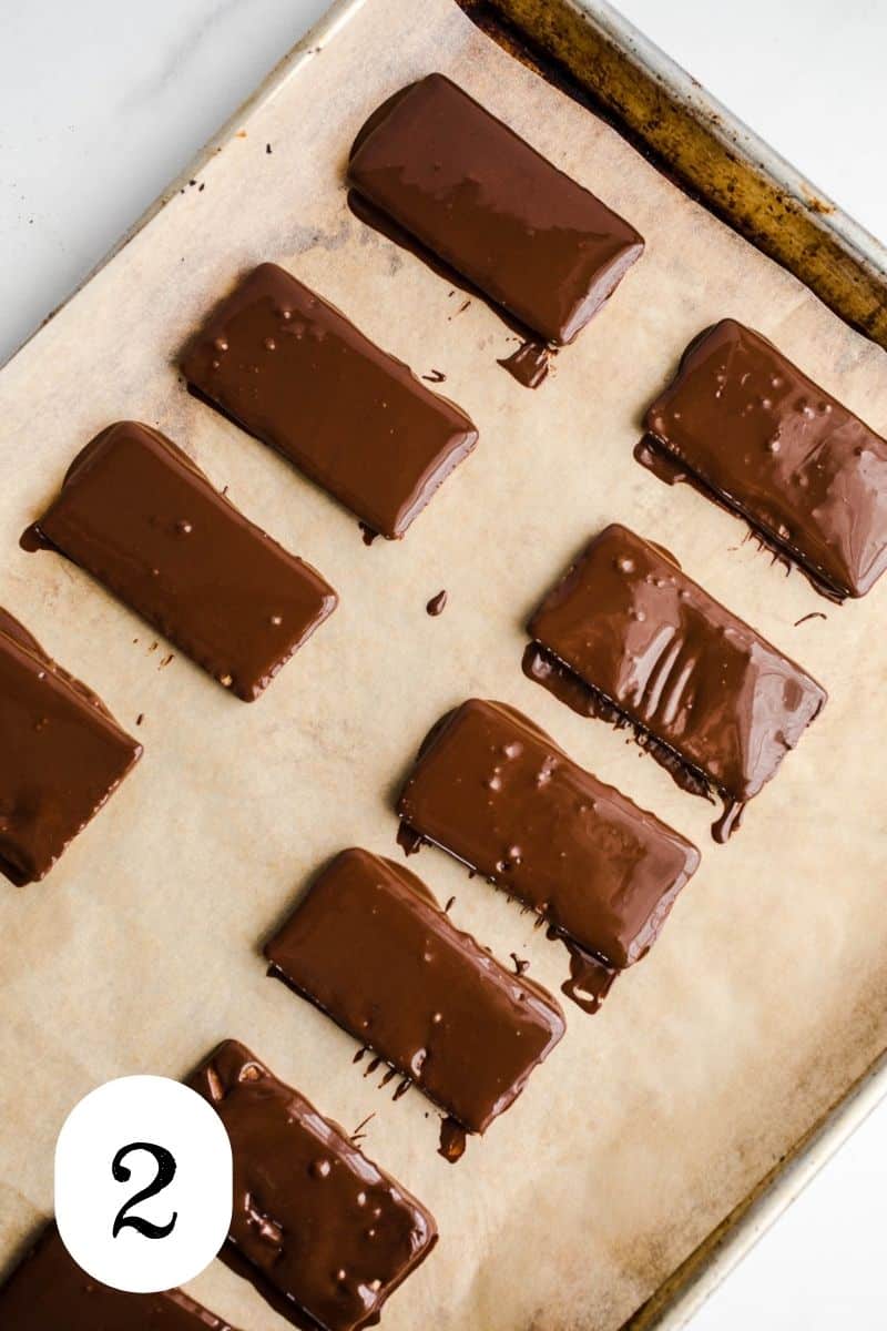 Chocolate dipped cookies in rows on a baking sheet.