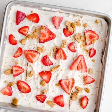 An icebox cake in a baking pan topped with strawberries and graham cracker crumbs.