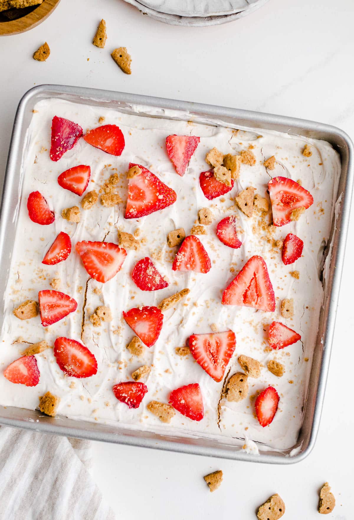 An icebox cake in a baking pan topped with strawberries and graham cracker crumbs.