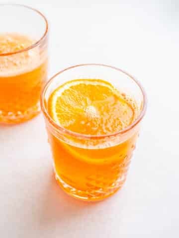 Two orange cocktails on a white surface.