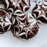 Chocolate cookies with a spiderweb glaze on a plate.