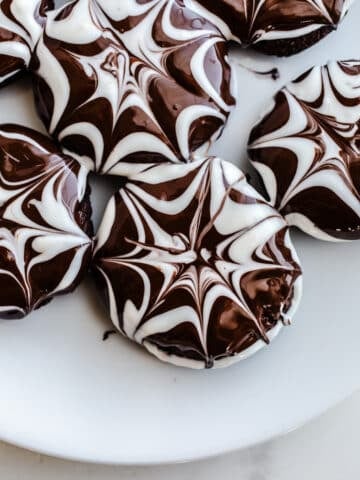 Chocolate cookies with a spiderweb glaze on a plate.