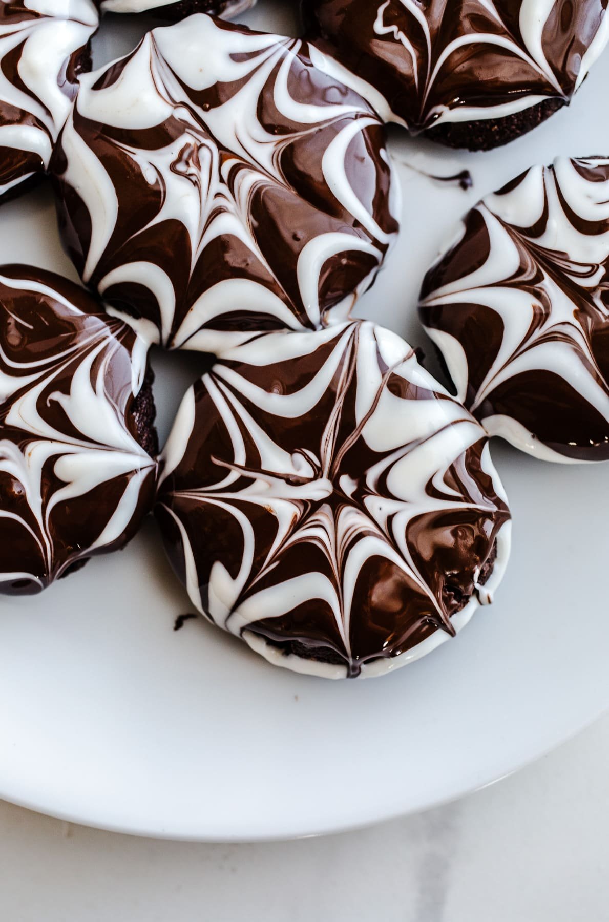 Chocolate cookies with a spiderweb glaze on a plate.