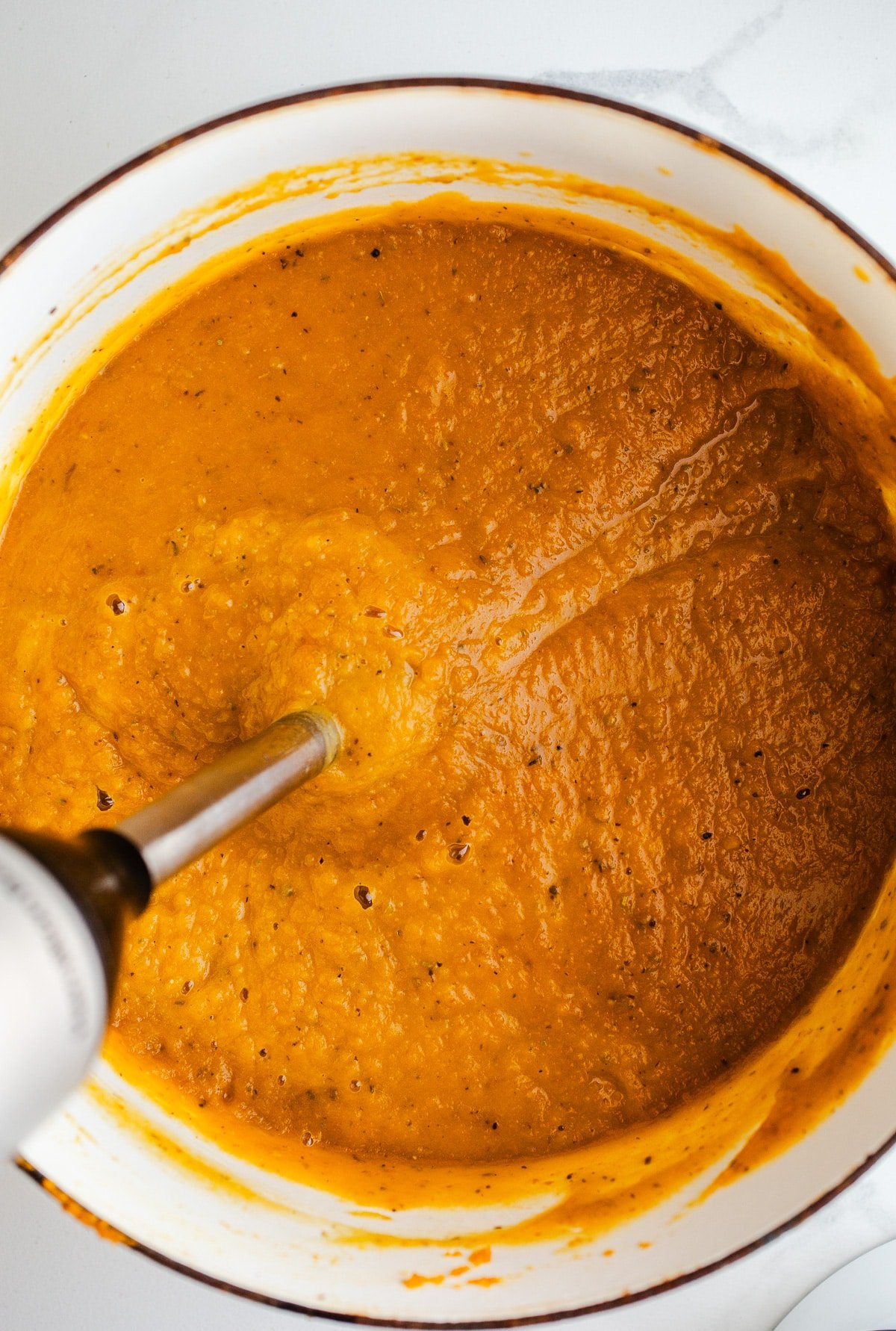 An immersion blender in a pot of soup.