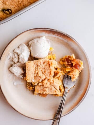 A piece of apple dump cake on a plate with ice cream.