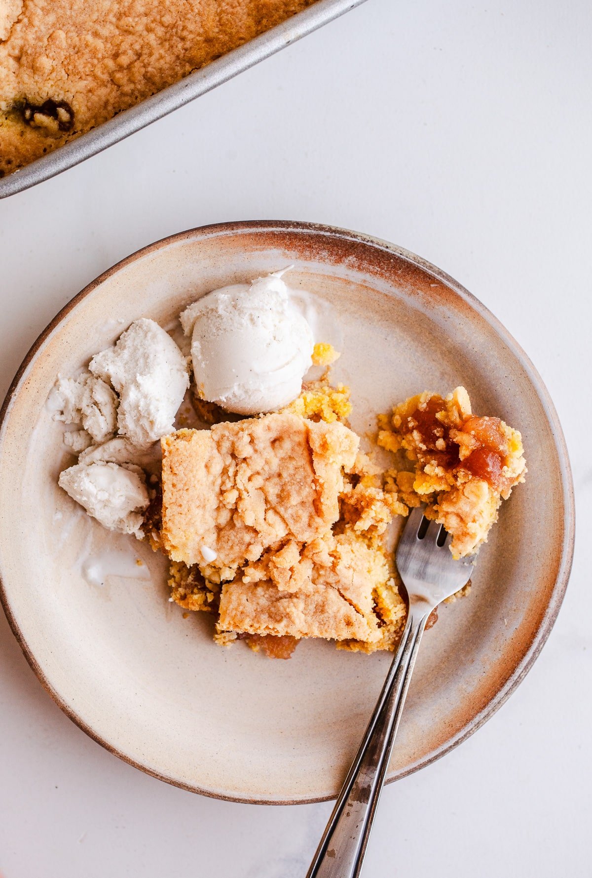 A piece of apple dump cake on a plate with ice cream.