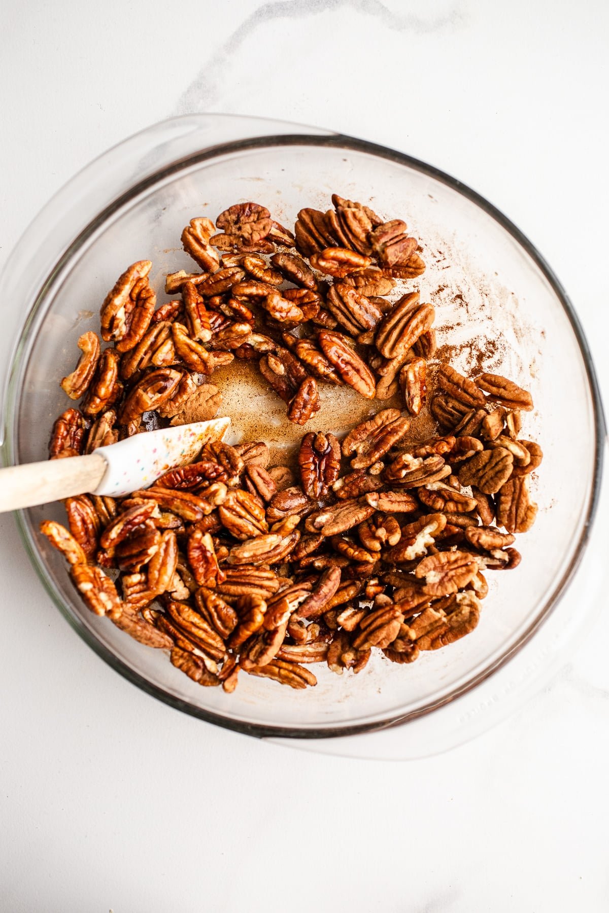 Pecans with spices and maple syrup in a mixing bowl.