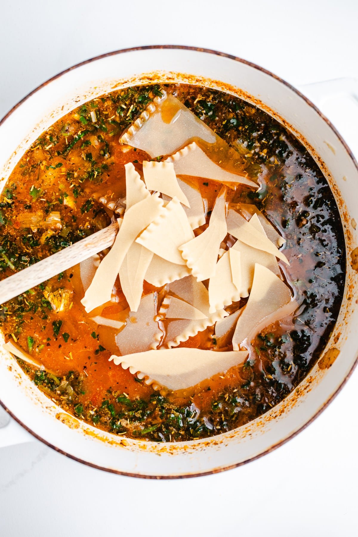 Dry lasagna noodles stirred into a pot. 