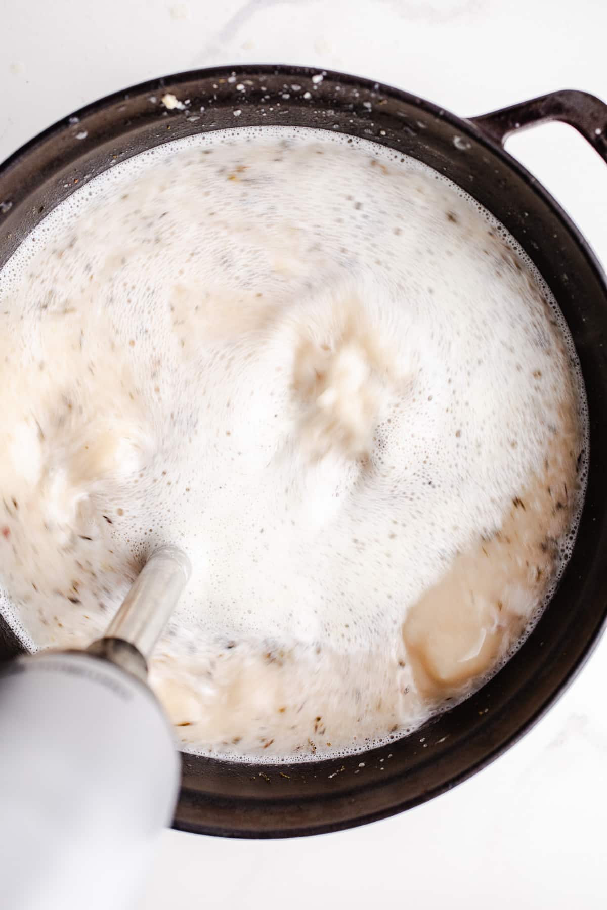 White bean soup being blended with an immersion blender.