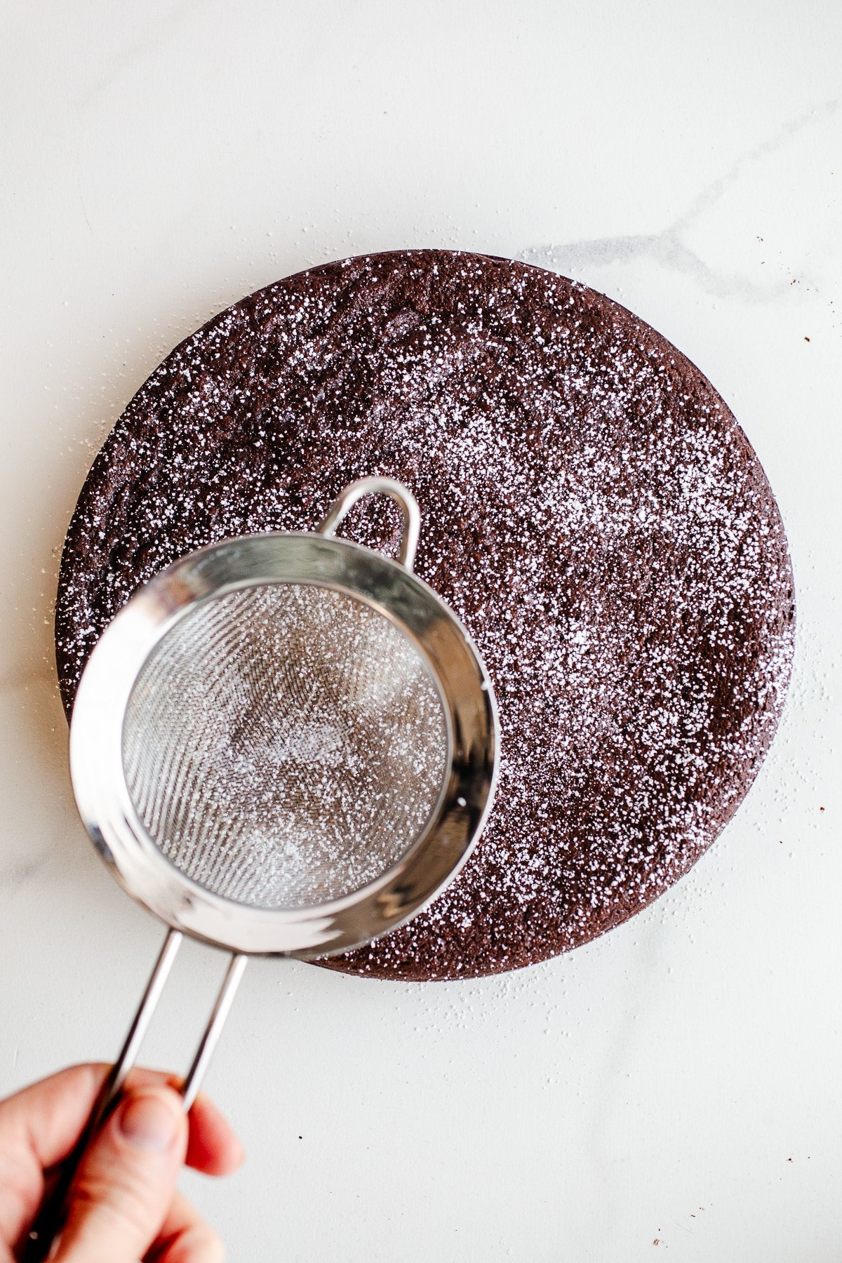 Chocolate cake being sprinkled with powdered sugar.