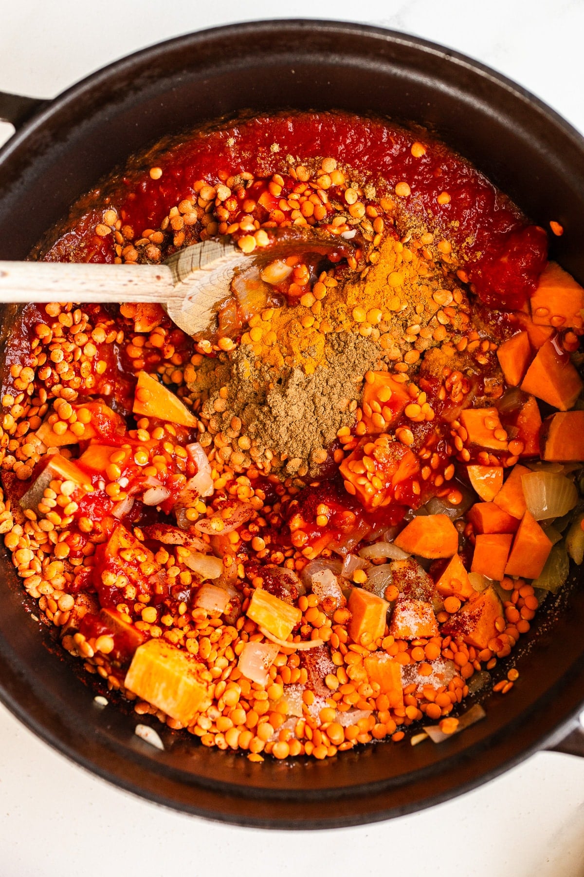 Ingredients for lentil soup in a black pot.