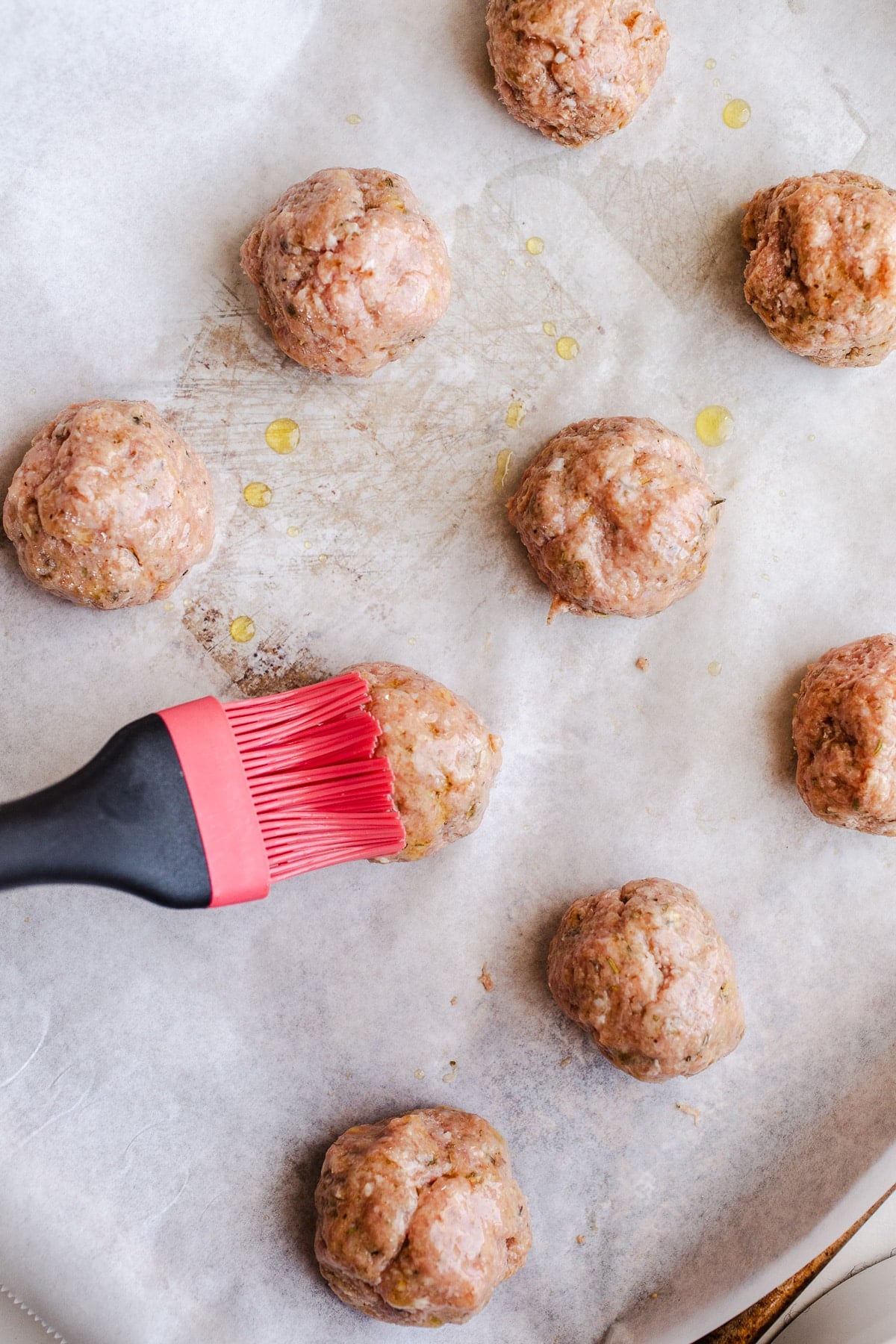 Olive oil being brushed on top of raw meatballs.