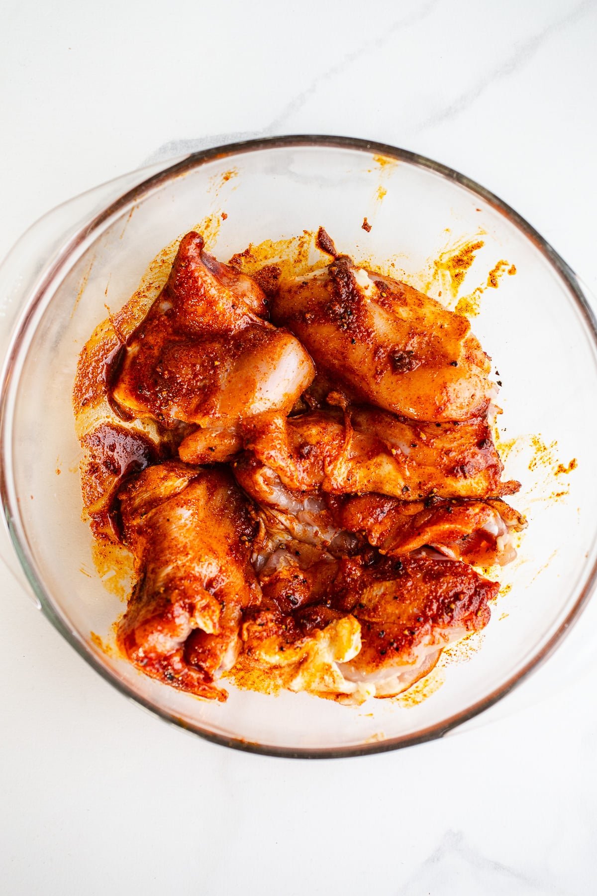Chicken and spices in a glass bowl.