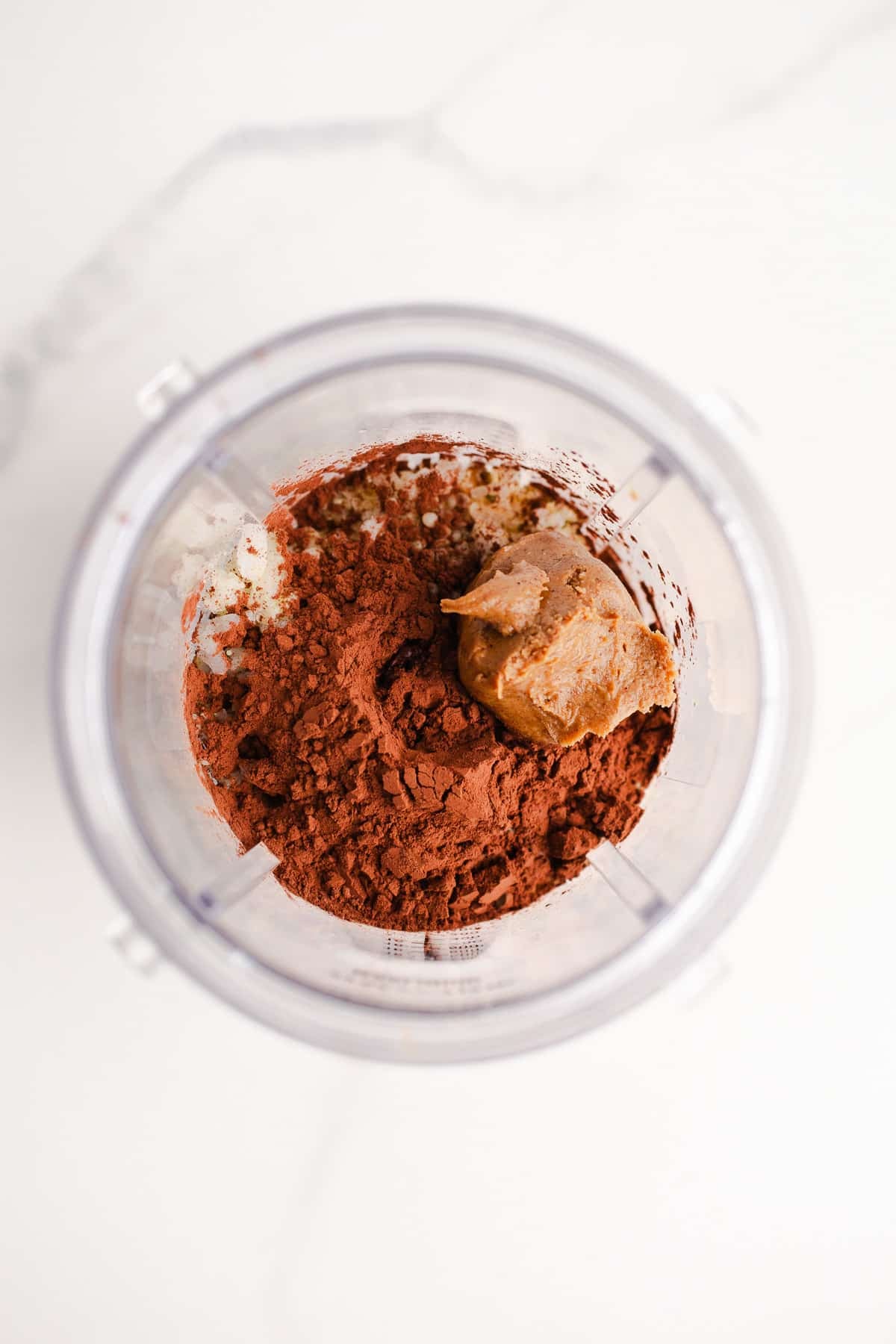 Cocoa powder and almond butter in a blender cup.