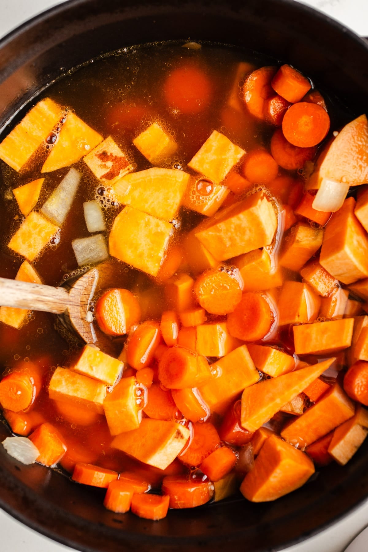 Carrots and sweet potatoes in a pot with broth.