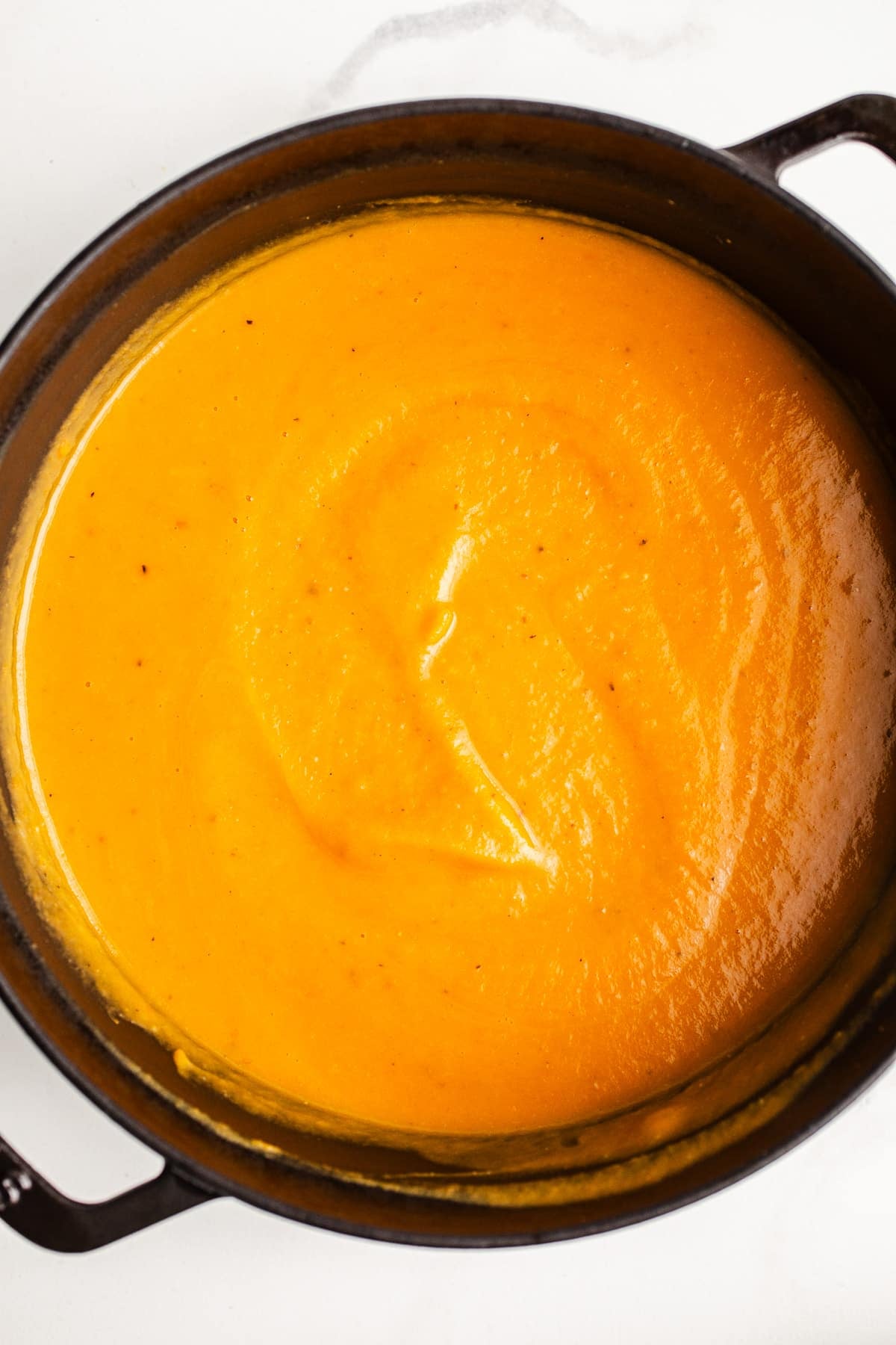 Sweet potato carrot soup in a large black pot.