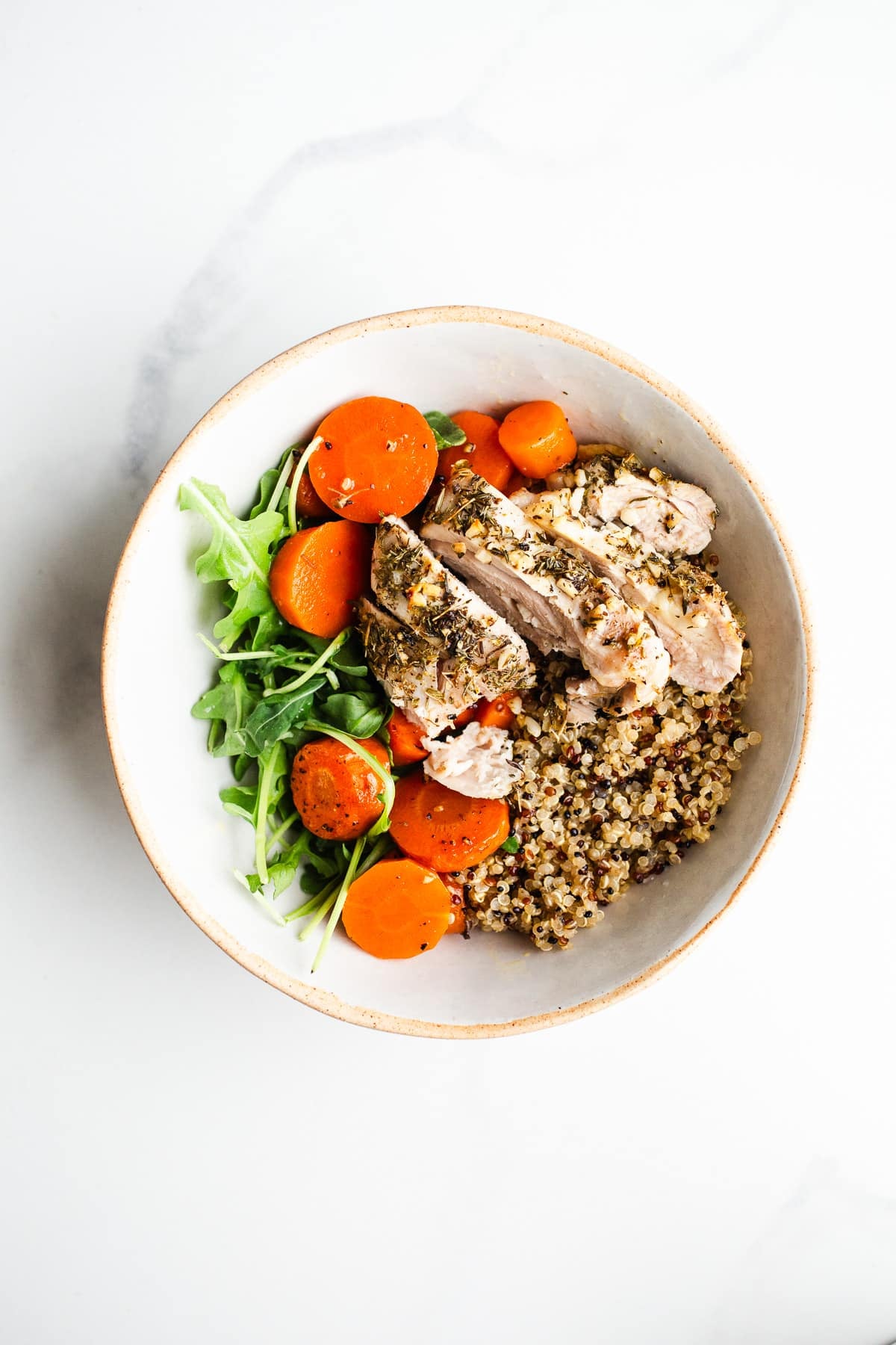 Sliced chicken and roasted carrots on quinoa in a bowl.
