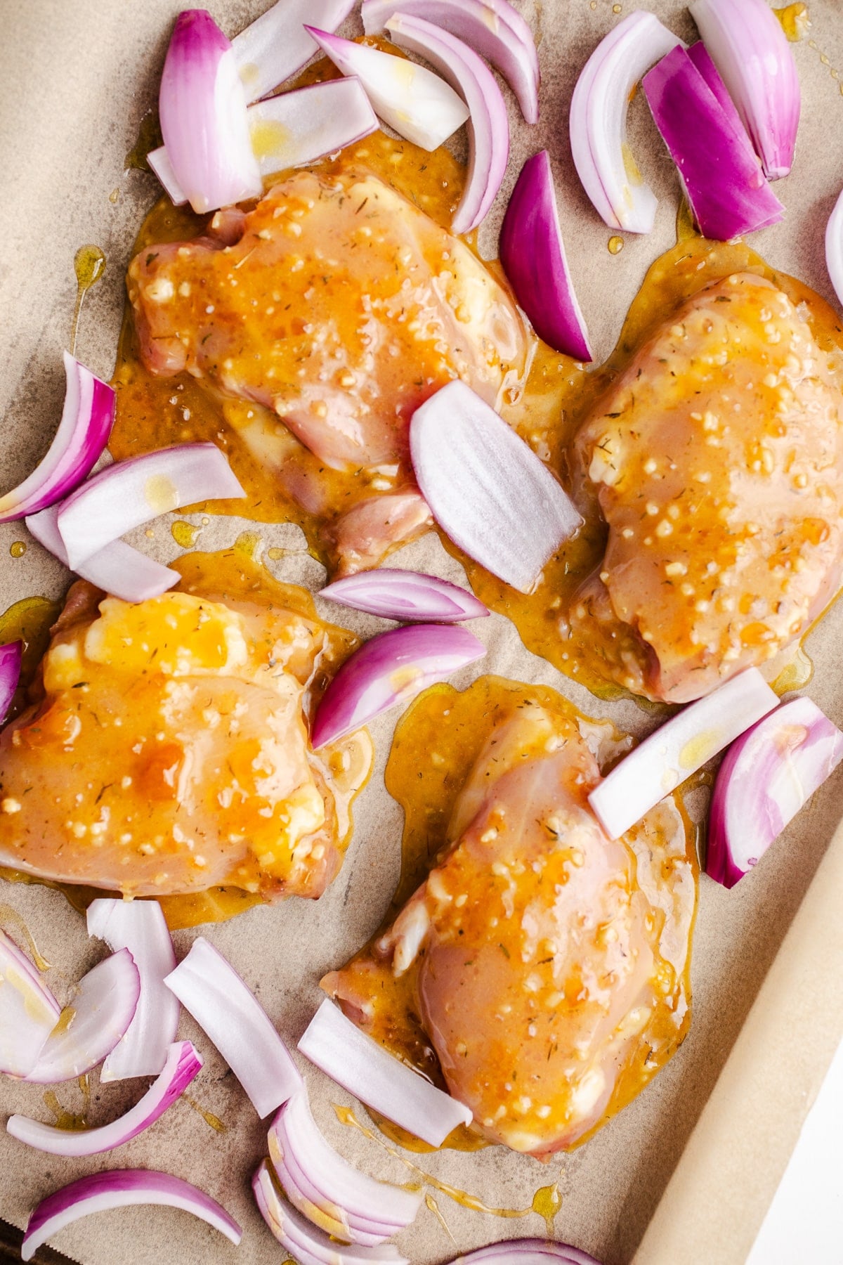Marinated chicken and raw red onions on sheet pan.