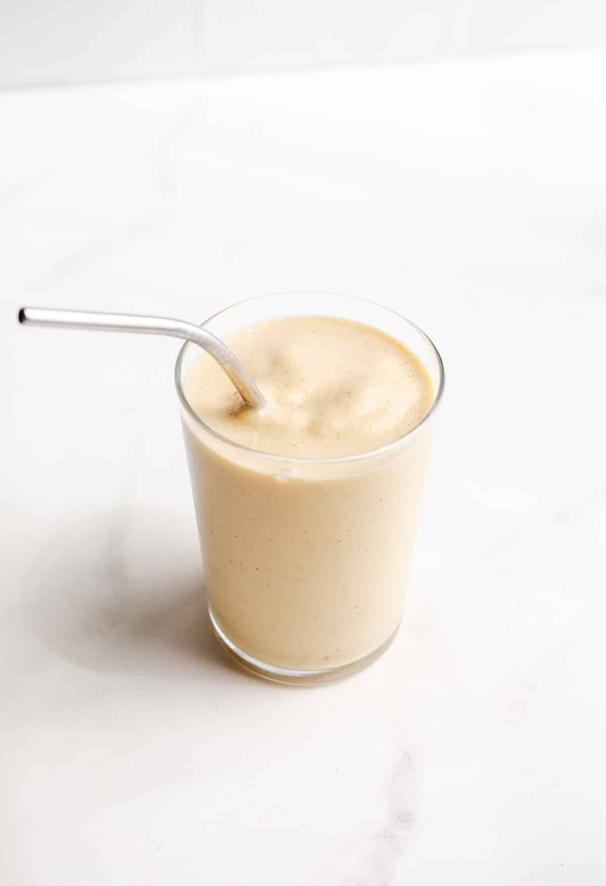 A peach banana smoothie in a glass with a straw.