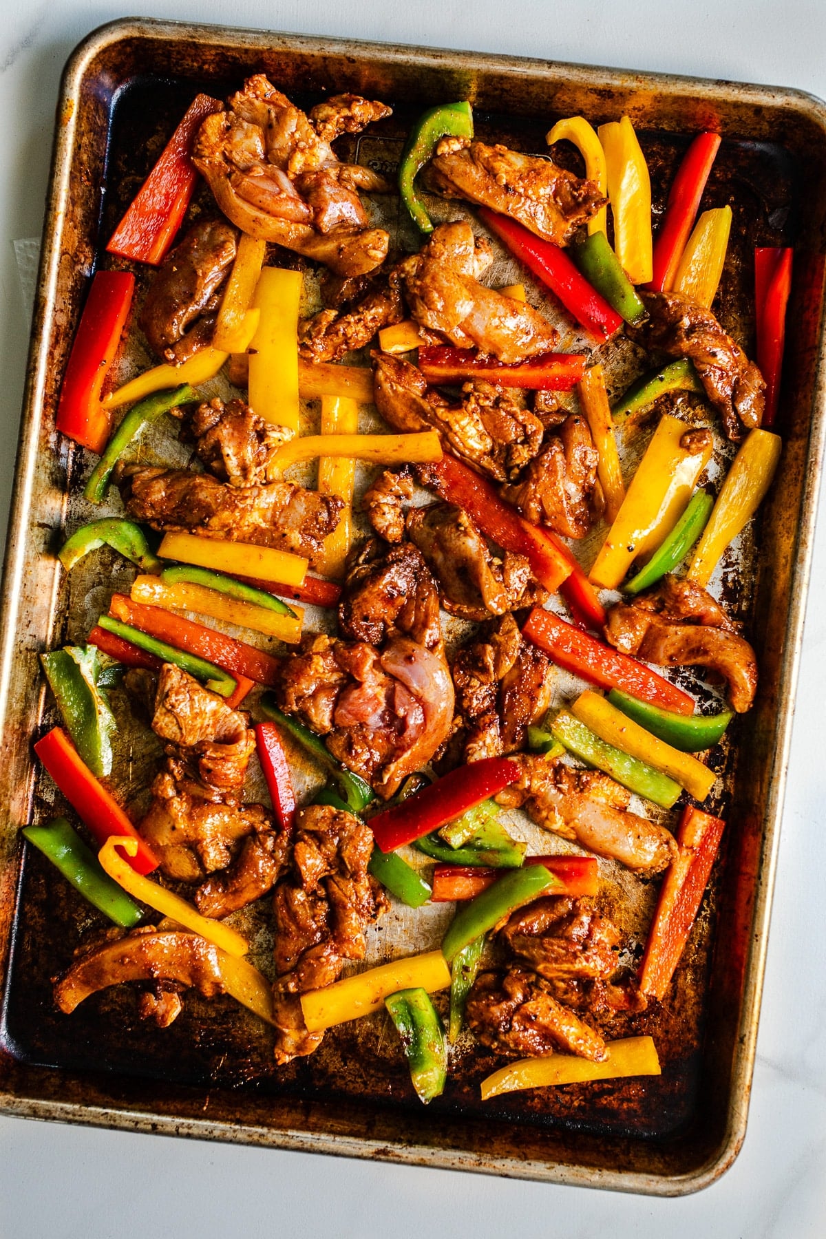 Raw chicken and bell peppers on a sheet pan.