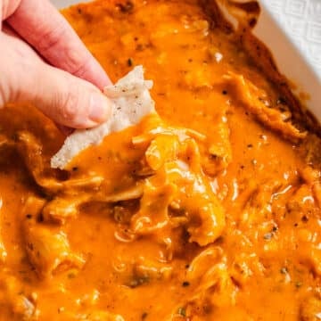 A chip scooping out buffalo chicken dip from a baking dish.