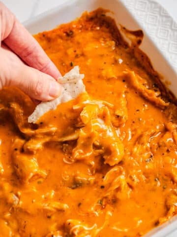 A chip scooping out buffalo chicken dip from a baking dish.