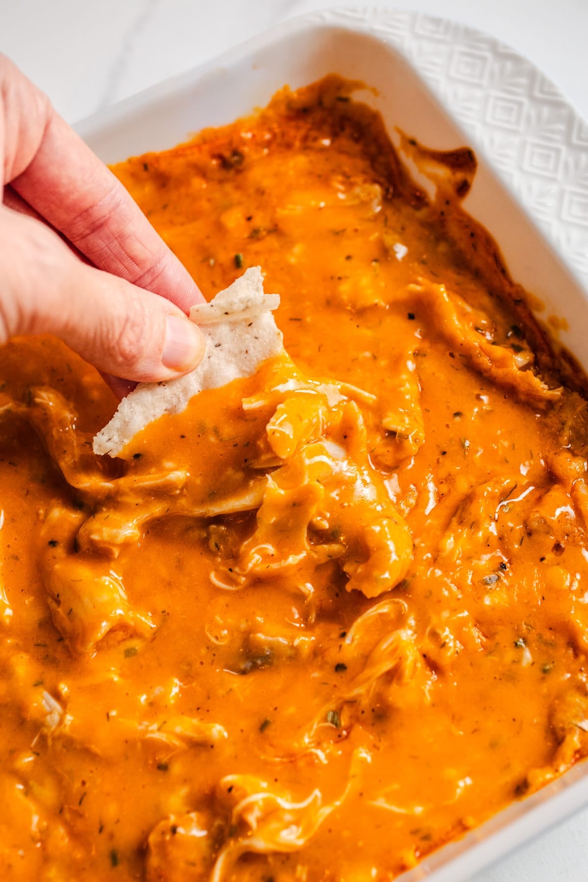 A chip scooping out buffalo chicken dip from a baking dish.